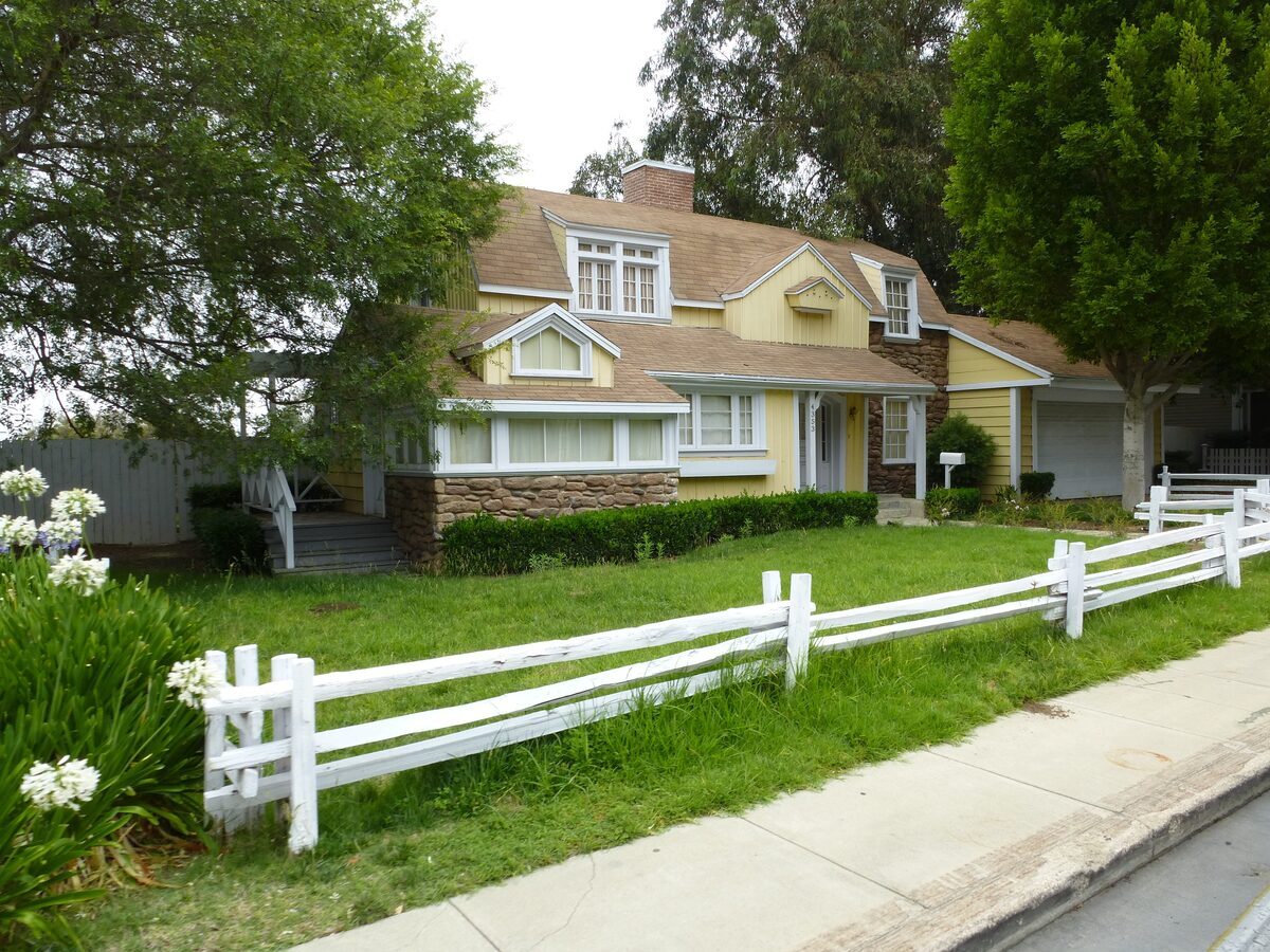 Charming yellow cottage-style home with rustic stone accents, a white post-and-rail fence, and a green front lawn, representing residential properties inspected by Northmark Property Inspections in De Pere, WI.
