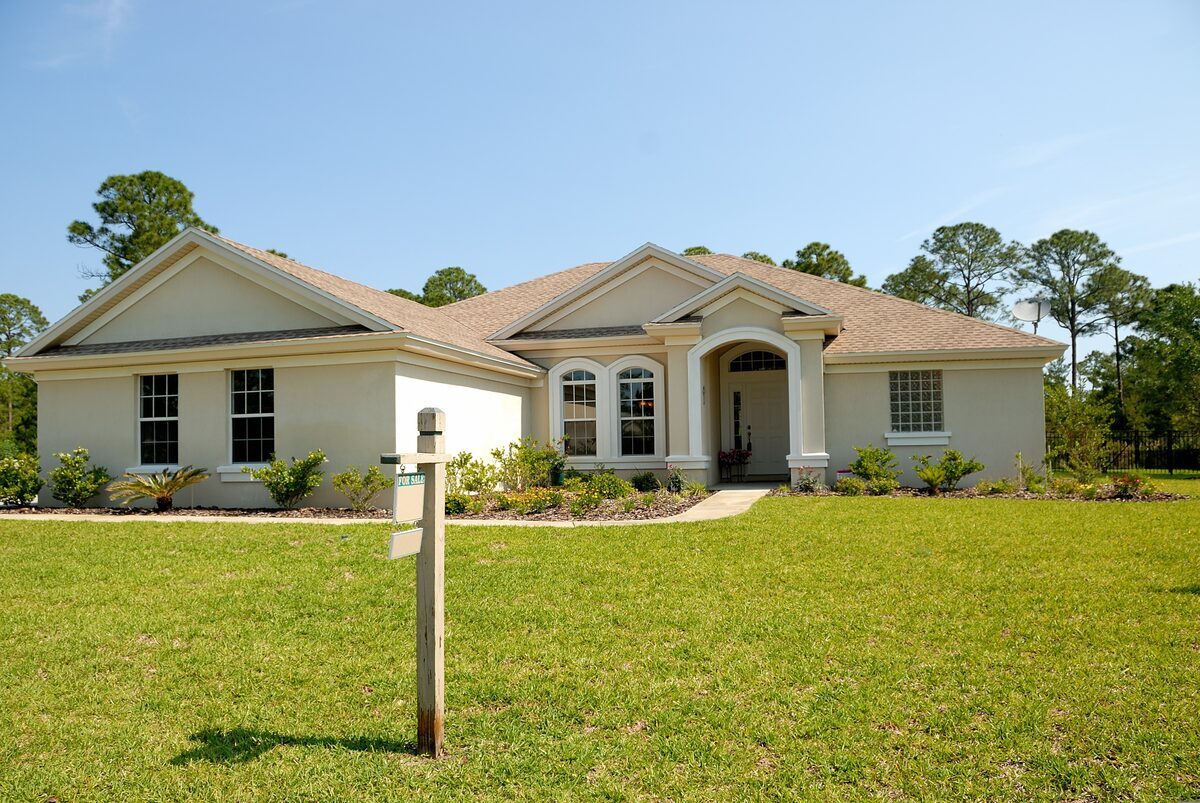 Modern stucco ranch-style home featuring a gabled roofline, front entryway arch, and a grassy front lawn with a real estate sign, representing residential properties inspected by Northmark Property Inspections in Gillett, WI.