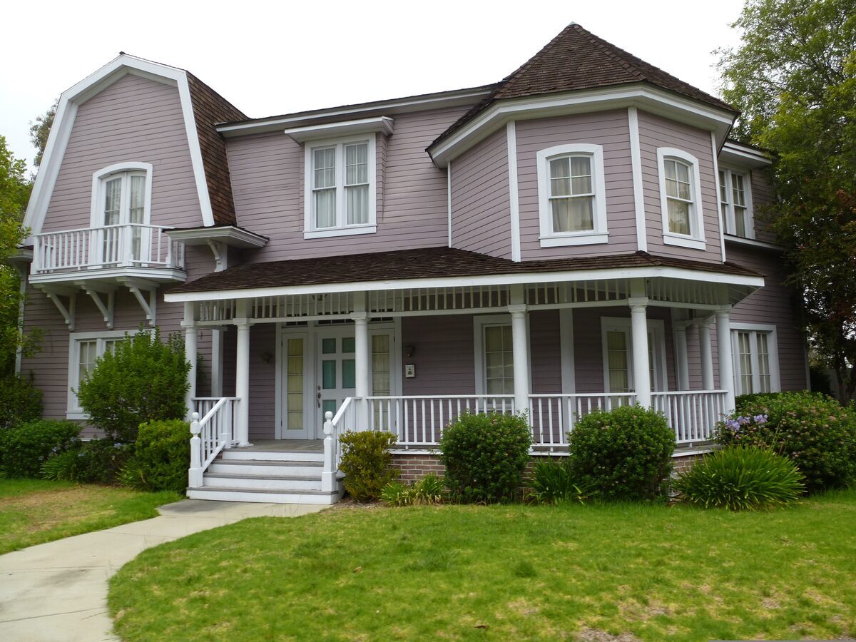 Historic Victorian-style home featuring light purple-gray siding, a grand wrap-around front porch with white columns, and distinct architectural gables, representing residential properties inspected by Northmark Property Inspections in Oconto, WI.