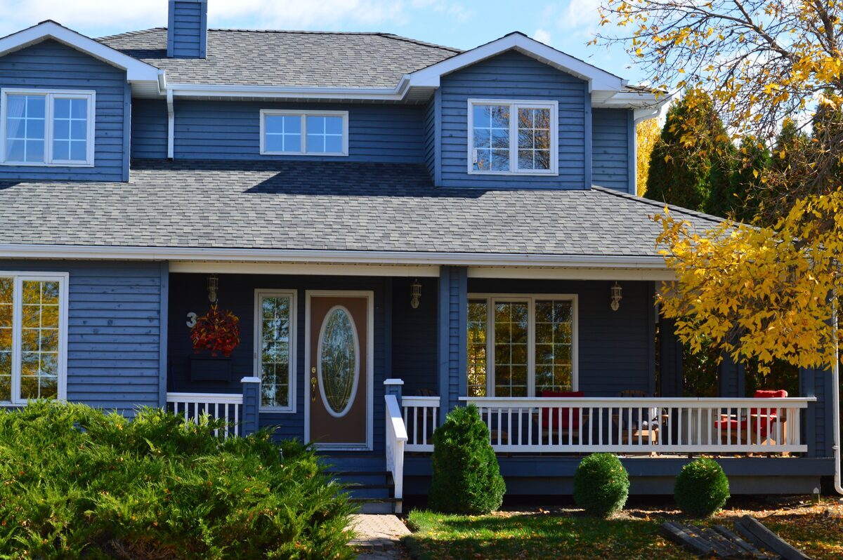 Charming blue two-story home featuring horizontal siding, a spacious front porch with white railings, and neat landscaping, representing residential properties inspected by Northmark Property Inspections in Peshtigo, WI.