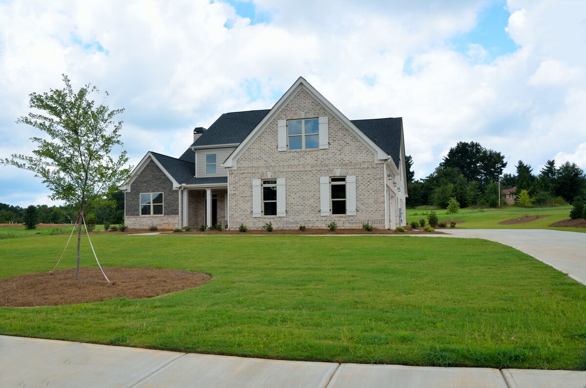 Modern multi-gabled home featuring a light-colored brick facade, dark shingles, and white decorative window shutters on a manicured green lawn, representing residential properties inspected by Northmark Property Inspections in Pulaski, WI.