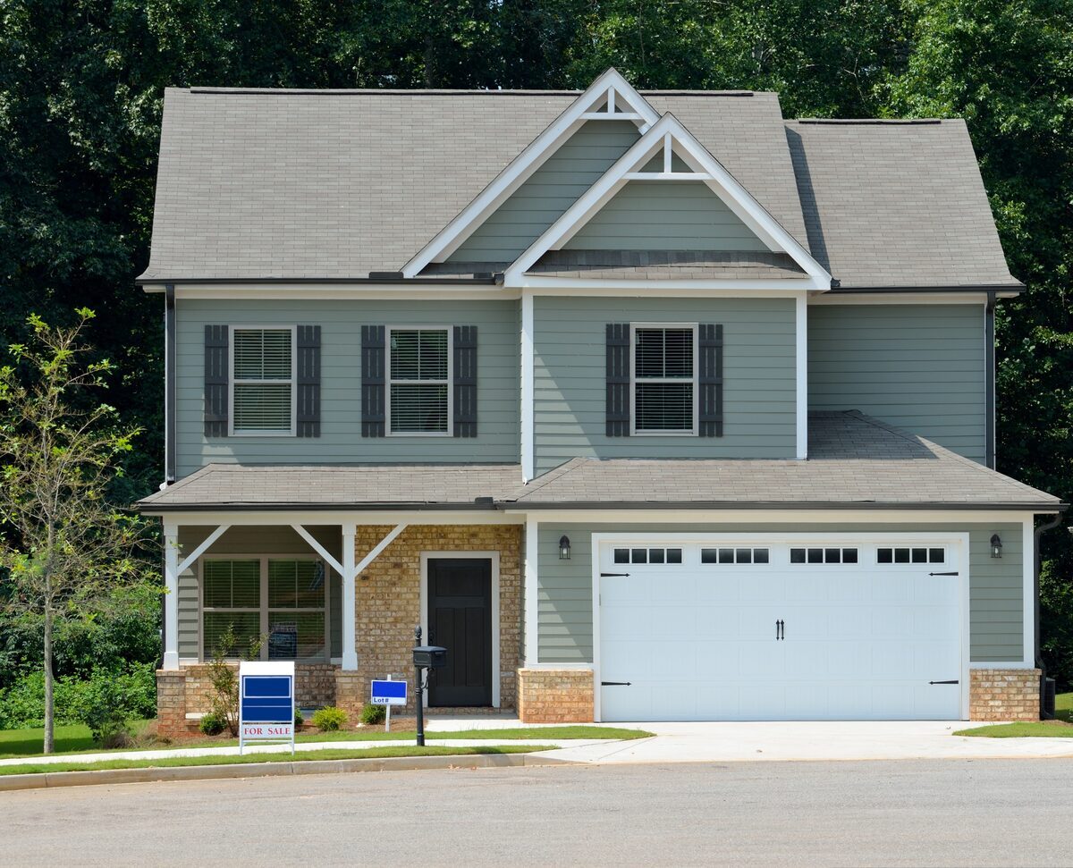 Modern sage green two-story home featuring an attached garage, dark window shutters, and a brick entryway facade, representing residential properties inspected by Northmark Property Inspections in Shawano, WI.